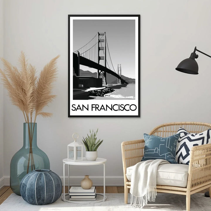 Living room with a framed picture of the Golden Gate Bridge labeled 'San Francisco', a vase with dried plants, a side table with a lantern and plant, and a wicker chair with pillows.
