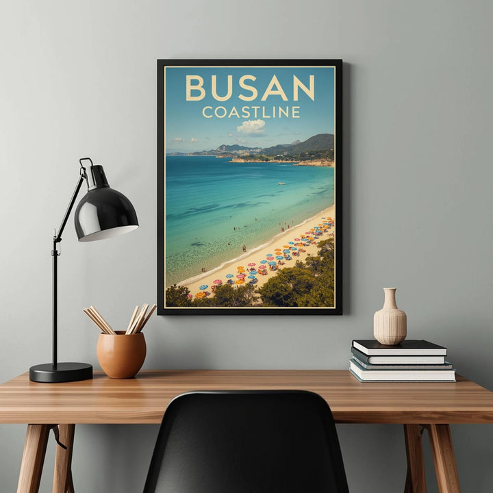 Framed artwork of Busan Coastline on a wall above a desk with a lamp and books.
