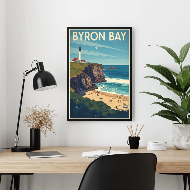 Framed Byron Bay poster on a wall above a desk with a lamp and plant.