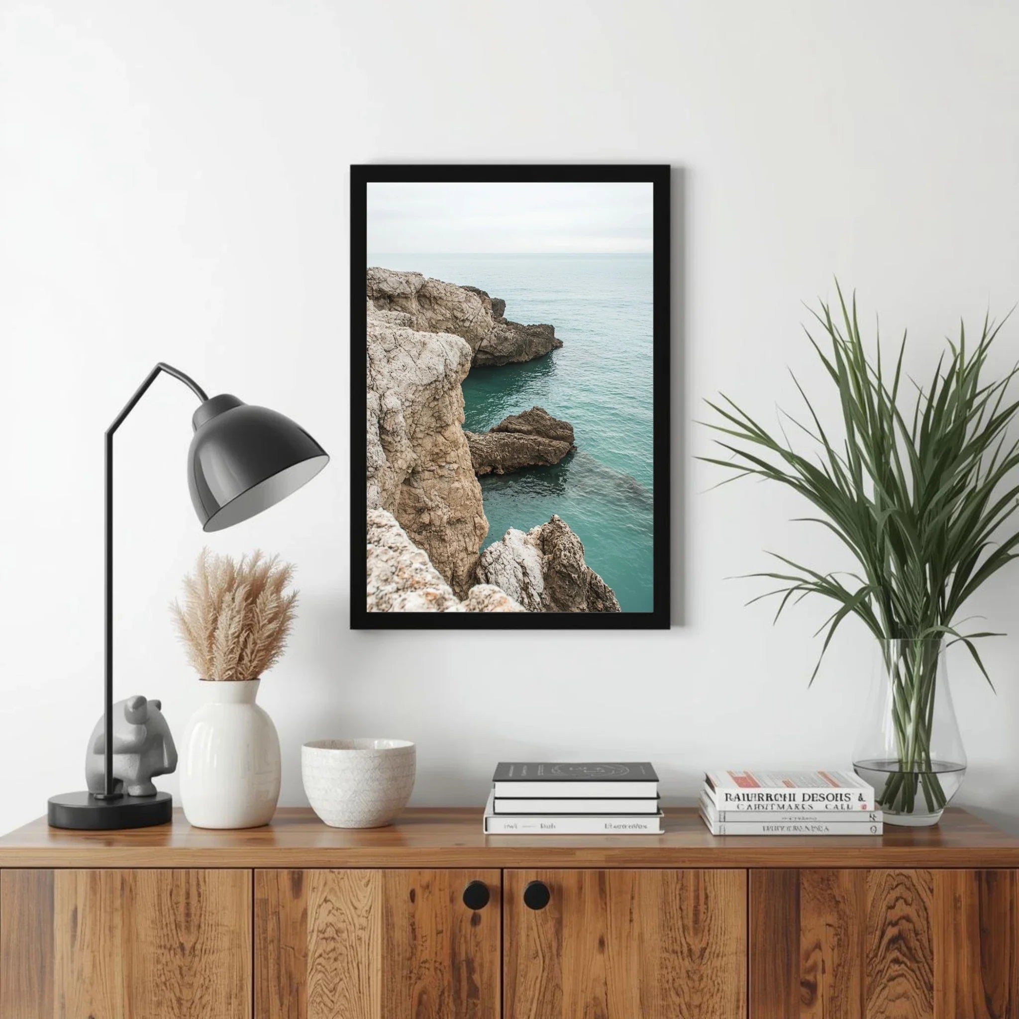 Framed artwork of a coastal scene on a wall above a wooden cabinet with decorative items.