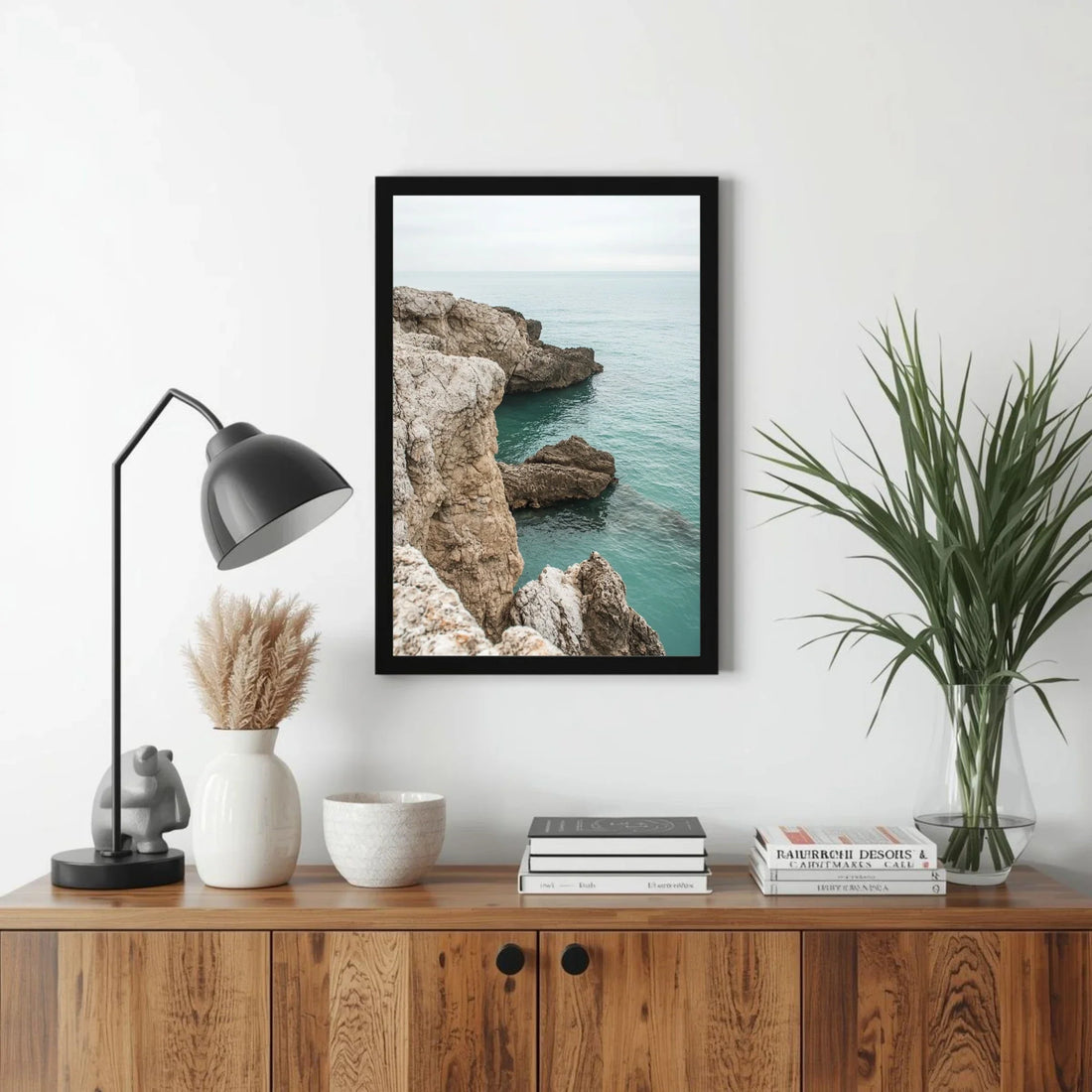 Framed artwork of a coastal scene on a wall above a wooden cabinet with decorative items.