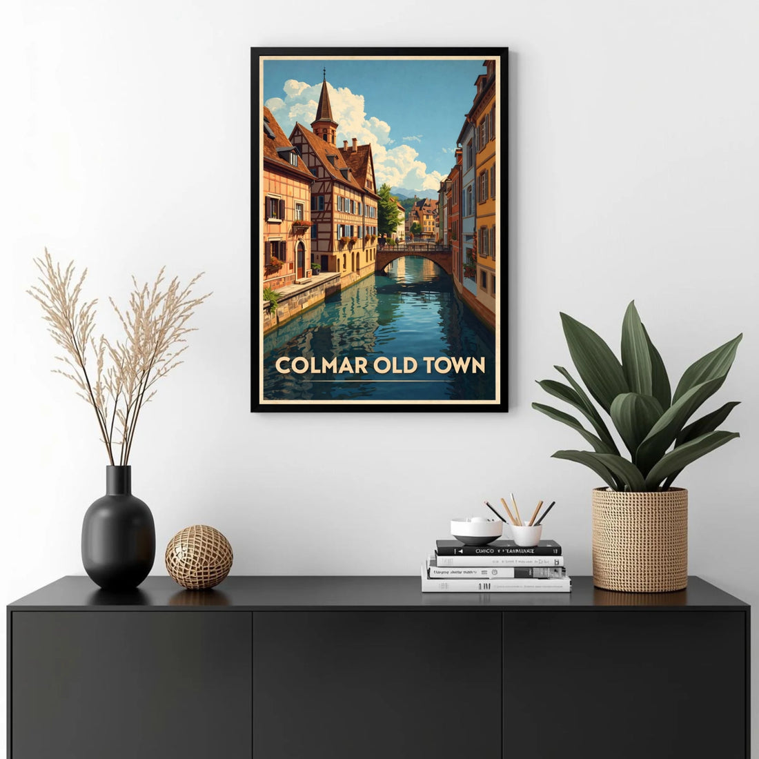 Framed artwork of Colmar Old Town on a wall above a black cabinet with decorative items.