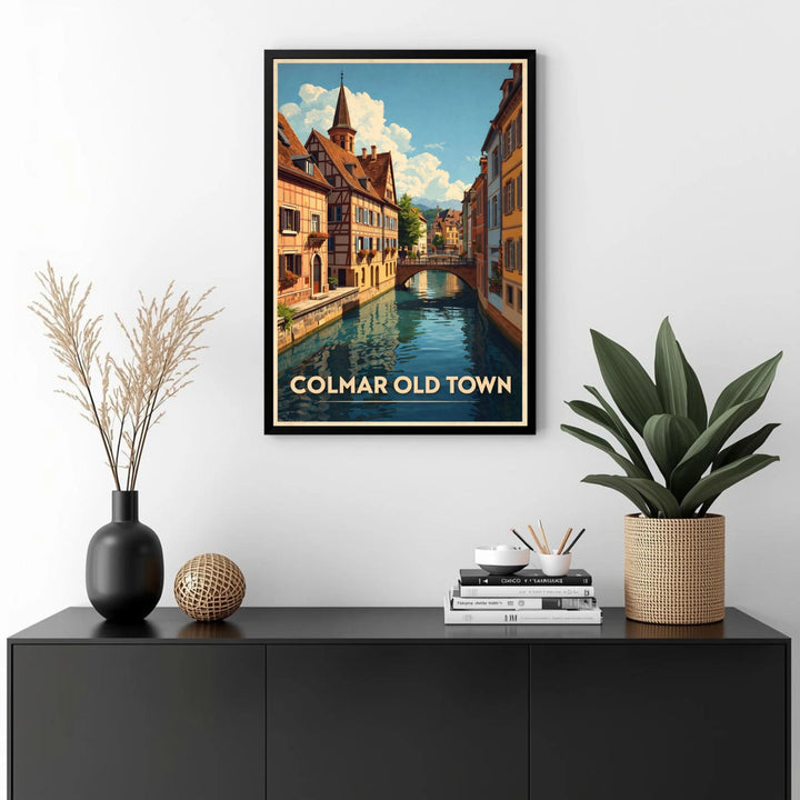 Framed artwork of Colmar Old Town on a wall above a black cabinet with decorative items.