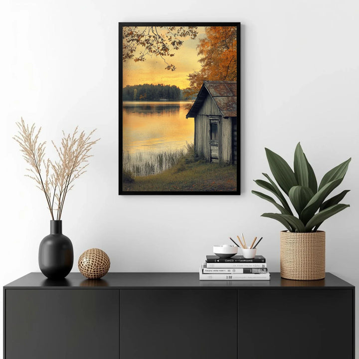 Framed artwork of a lake scene with a cabin above a black cabinet with decorative items.