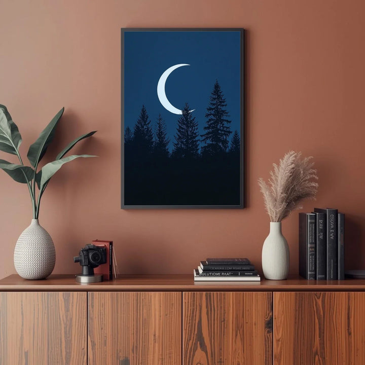 Framed artwork of a crescent moon over trees on a wall above a wooden cabinet with decor items.