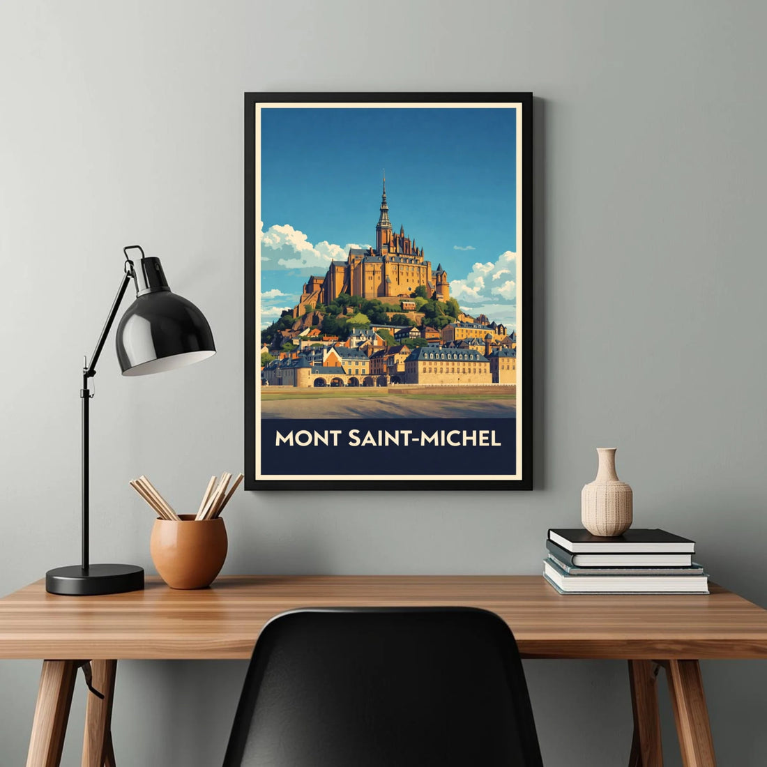 Framed poster of Mont Saint-Michel above a desk with a lamp and books.