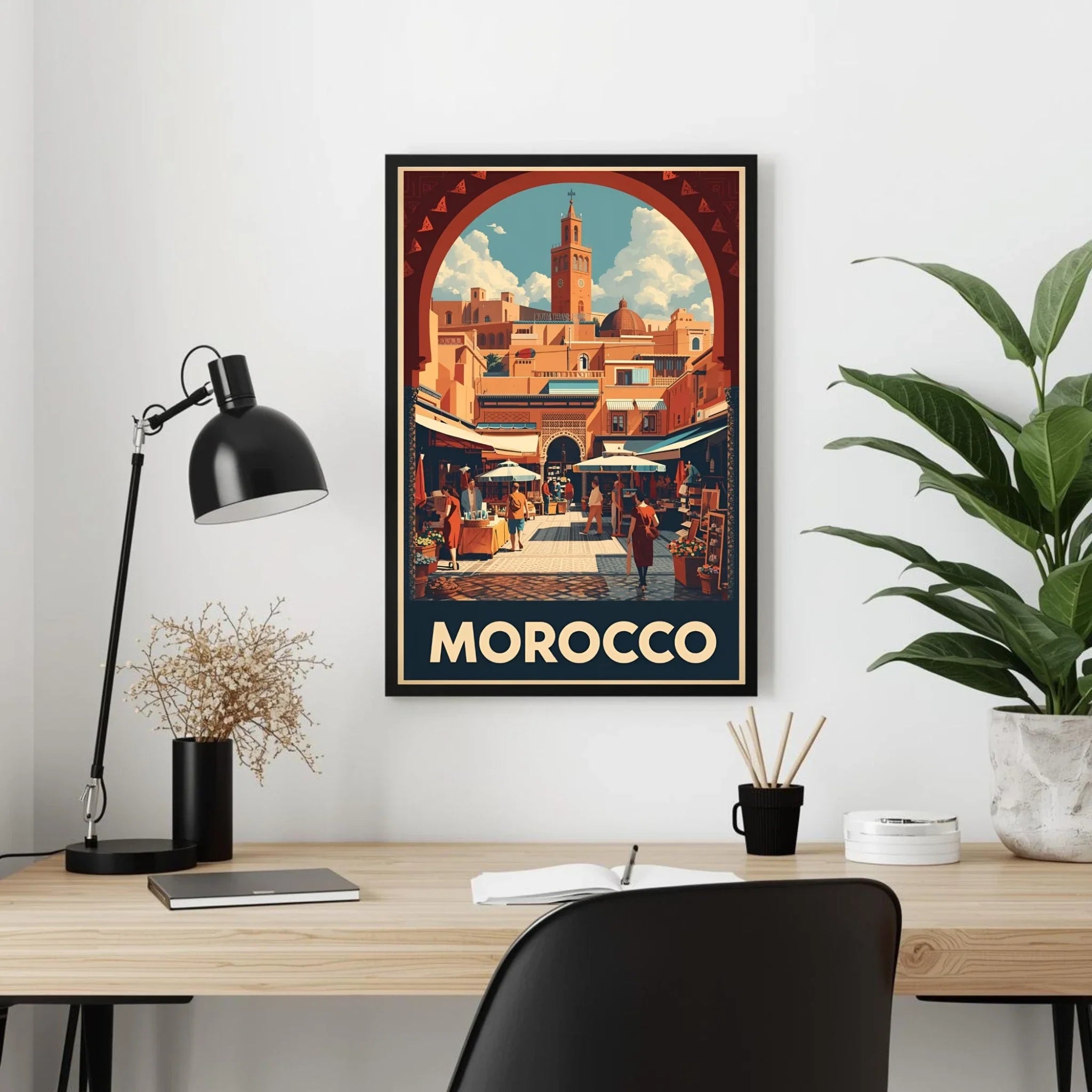 Framed 'Morocco' travel poster on a wall above a desk with a lamp and plant.