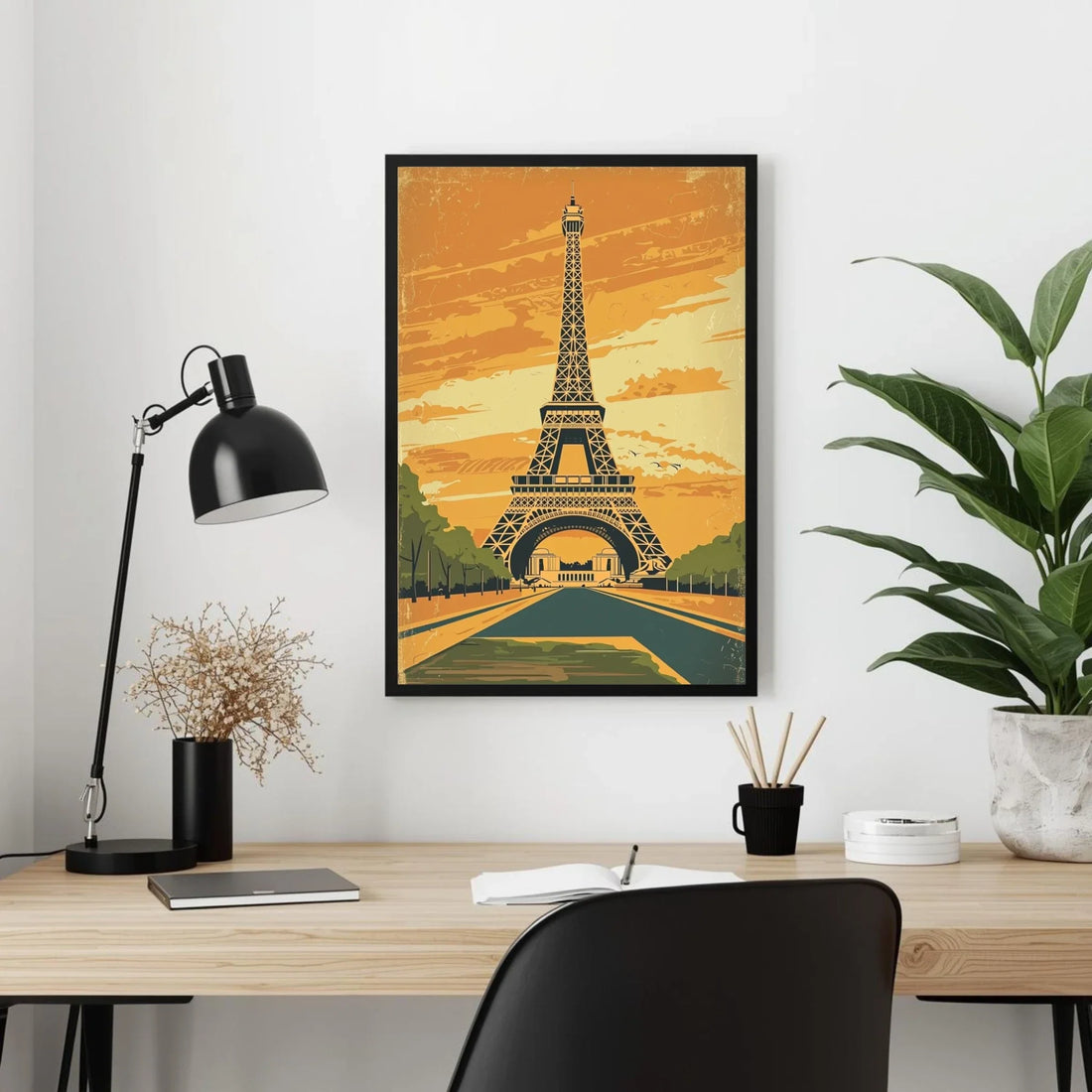 Framed Eiffel Tower poster on a wall above a desk with a lamp and plant.