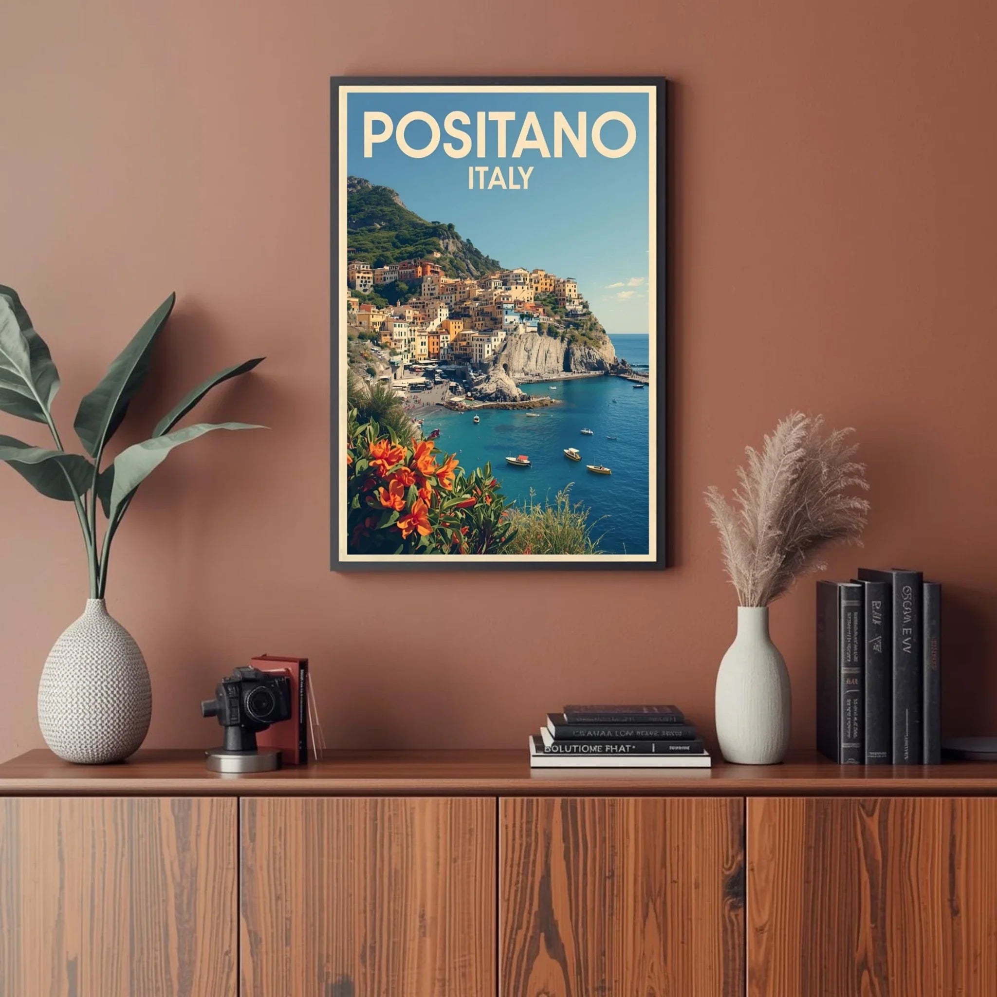 Framed poster of Positano, Italy on a wall above a wooden cabinet with decor items.