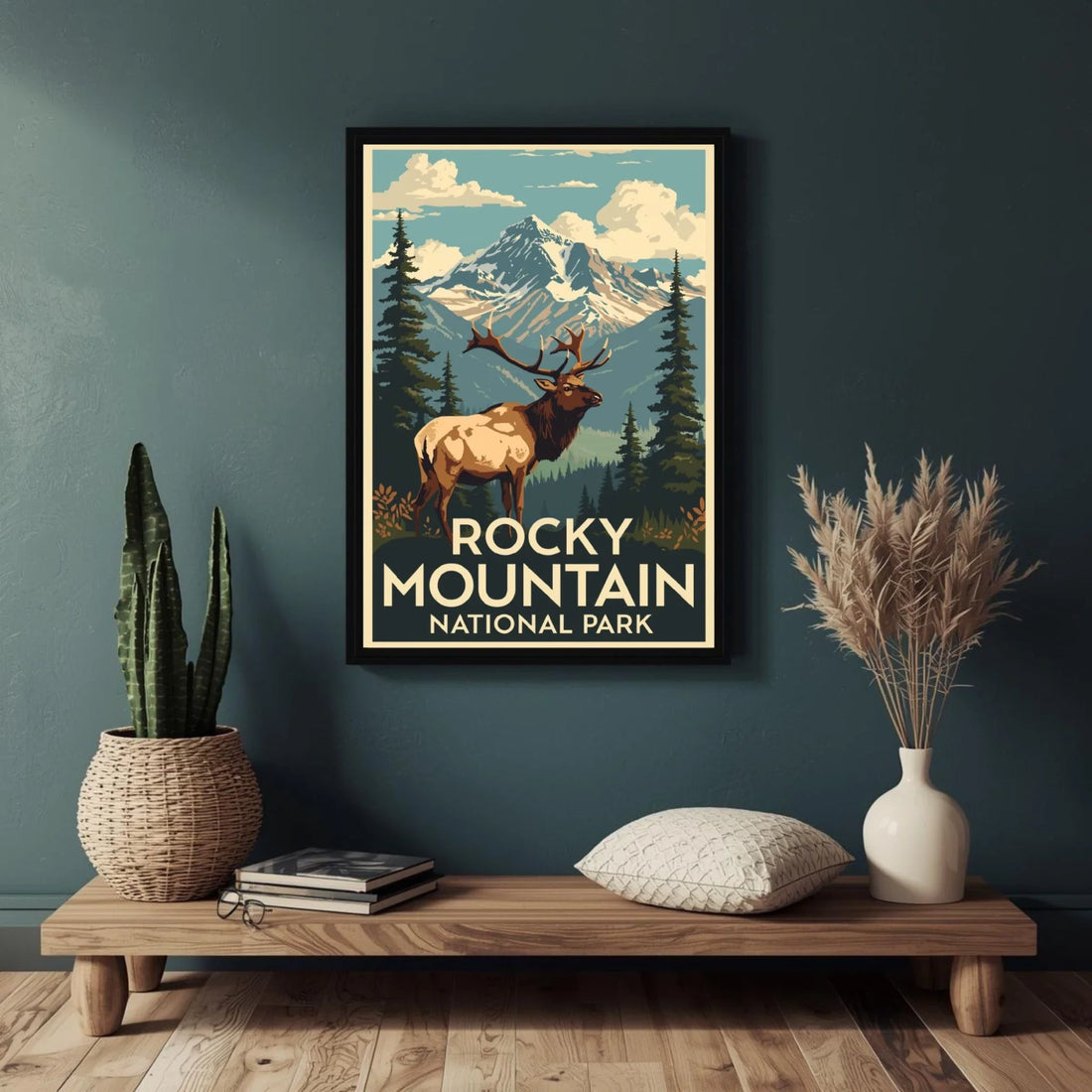 Framed poster of Rocky Mountain National Park with an elk on a dark green wall above a wooden shelf.