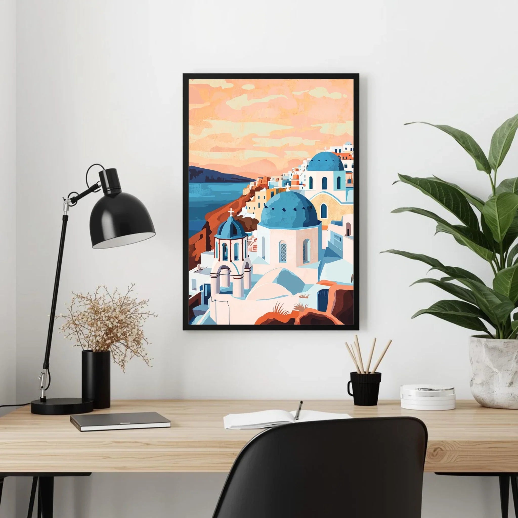 Framed artwork of a Mediterranean village on a desk with a lamp and plant.