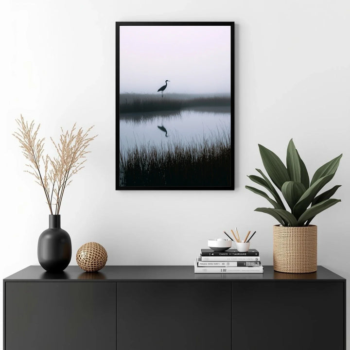 Framed artwork of a bird over water on a wall above a black cabinet with decorative items.