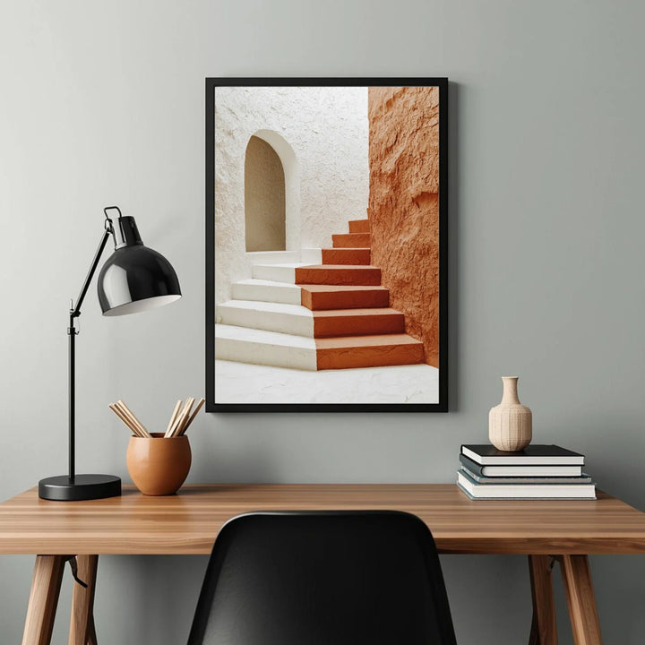 Framed artwork of a staircase on a wall above a desk with a lamp and decorative items.