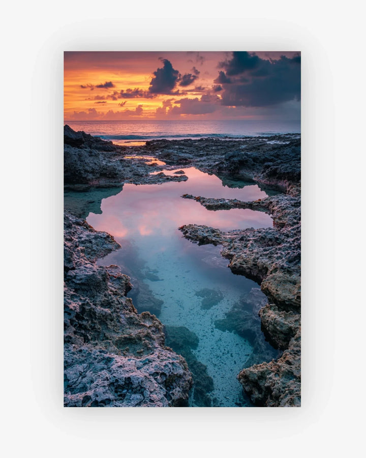 Sunset over a rocky coastline with clear water reflecting the colors of the sky.