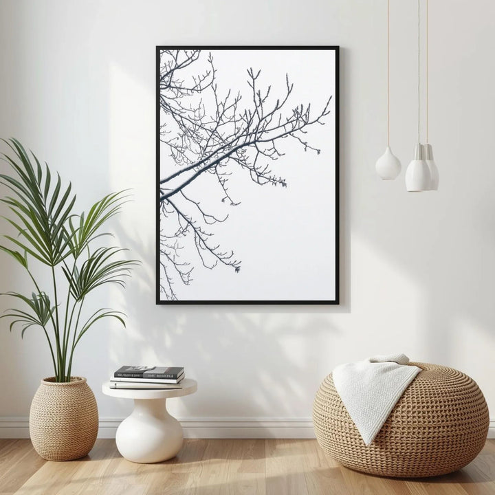 Modern interior with a framed black and white branch print, plant, and woven ottoman.