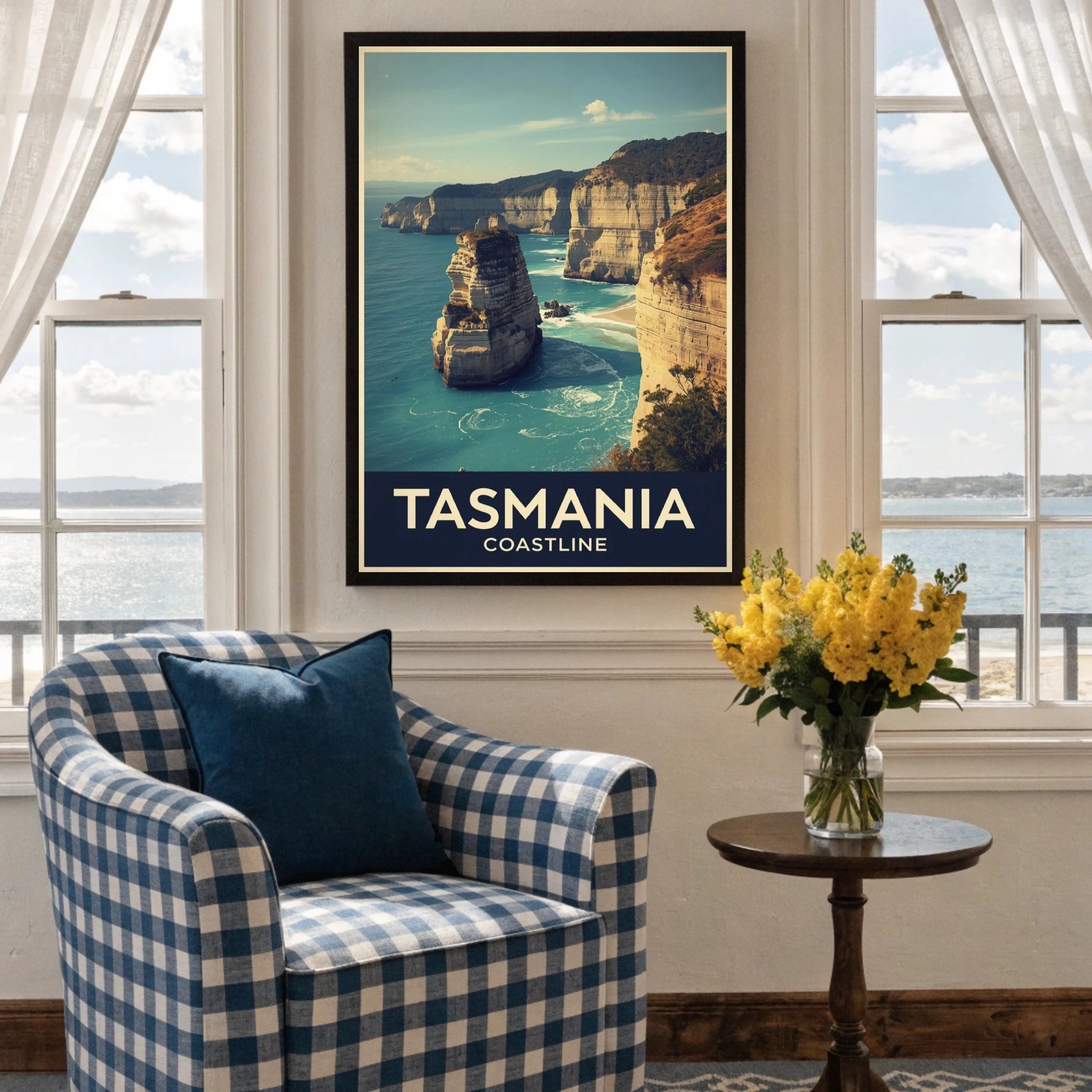 Framed poster of Tasmania coastline above a checkered armchair with a table and flowers in a room with large windows.