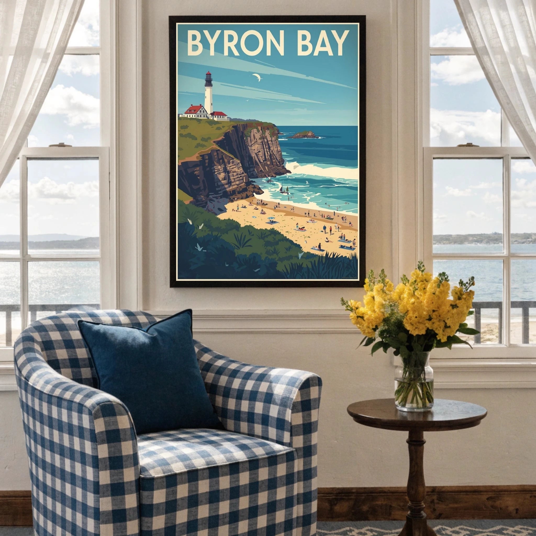 Framed artwork of Byron Bay on a wall above a checkered armchair with a table and flowers.