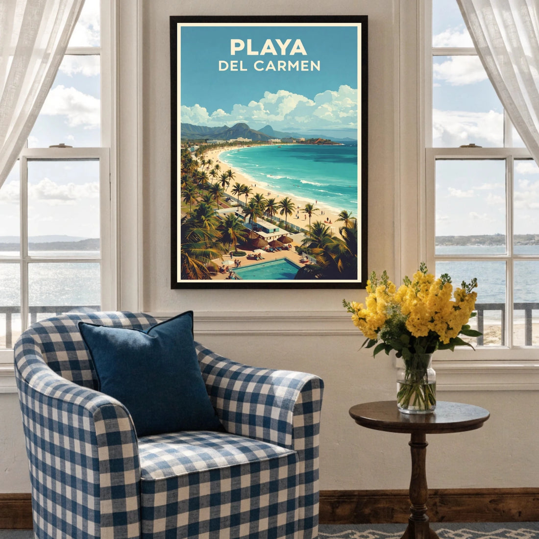 Framed artwork of Playa Del Carmen on a wall above a checkered armchair with a vase of yellow flowers.