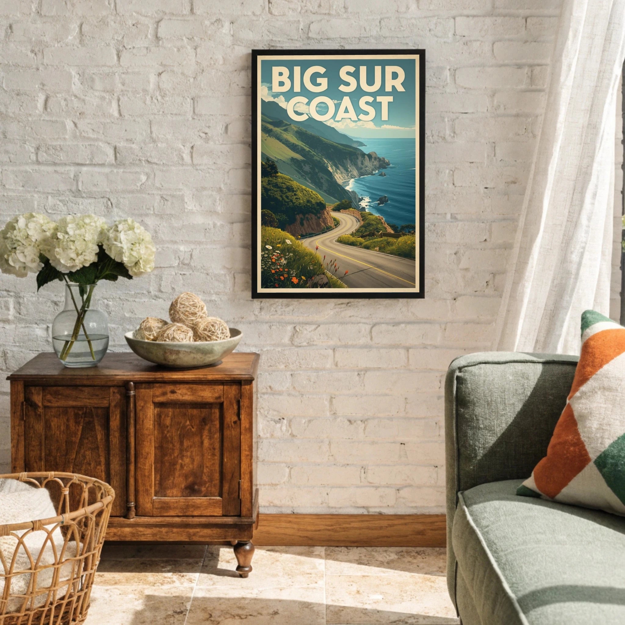 Living room with a 'Big Sur Coast' framed poster on the wall, wooden side table with flowers, and gray sofa.
